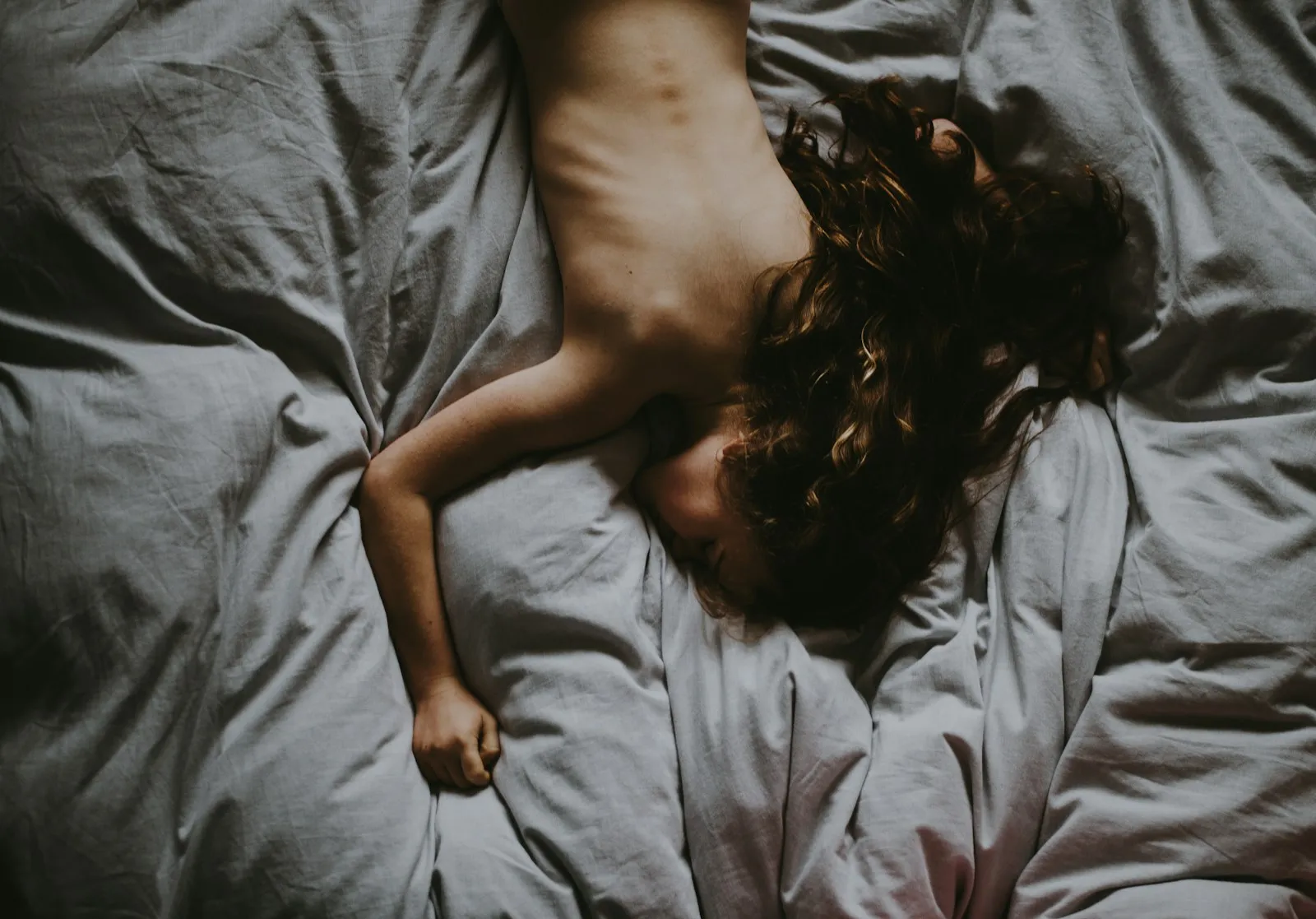 Woman lying on grey bedding, seen from above, her hair spread out