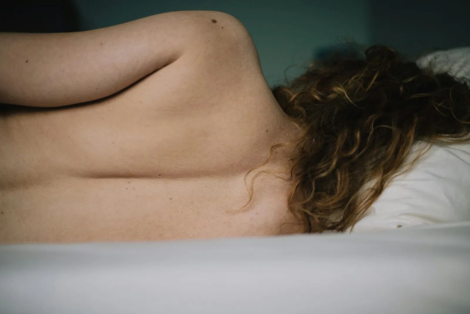 Woman lying face down, her curly hair across a white pillow