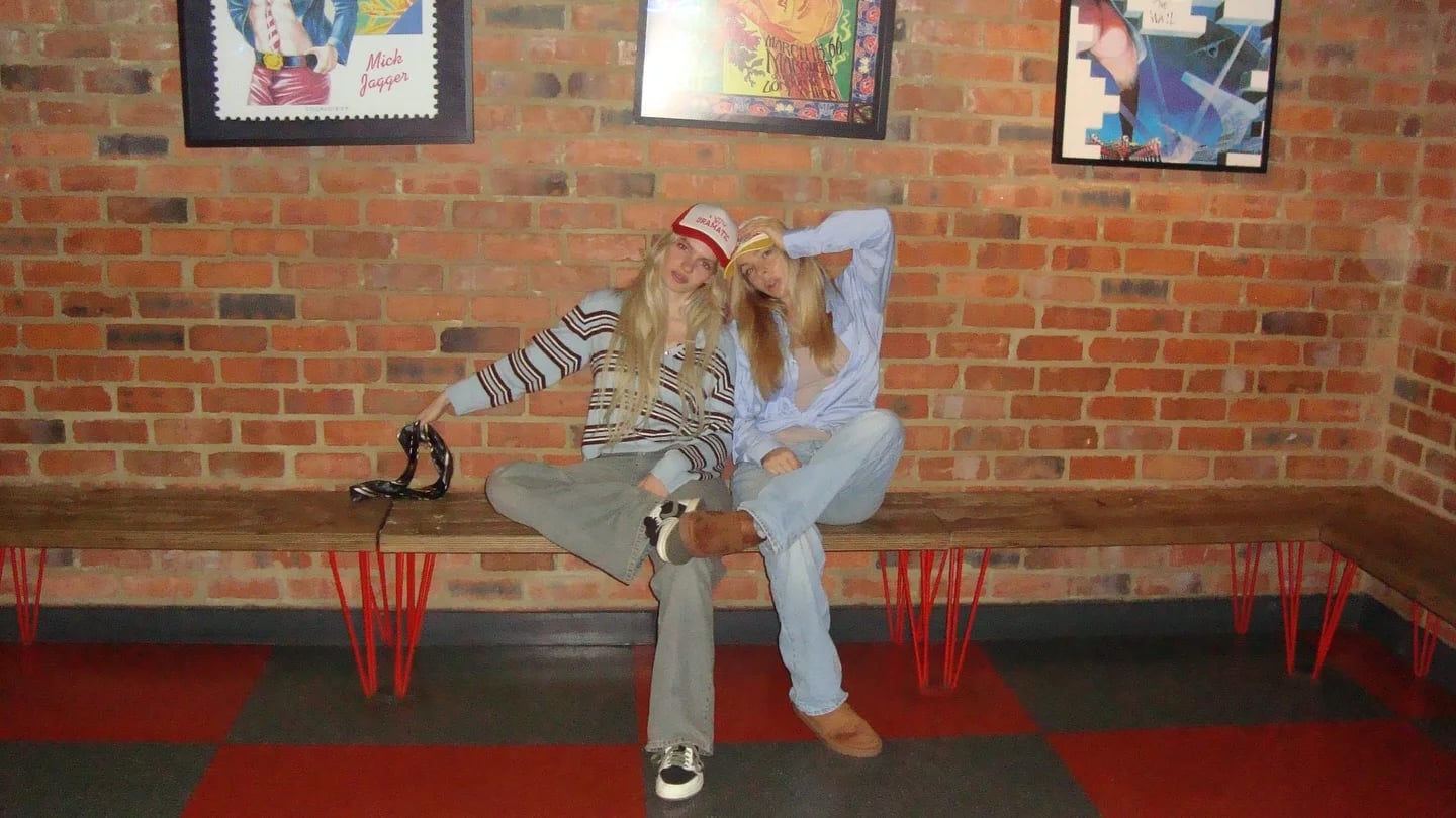 Woman in a denim outfit seated on a red bench against a brick wall