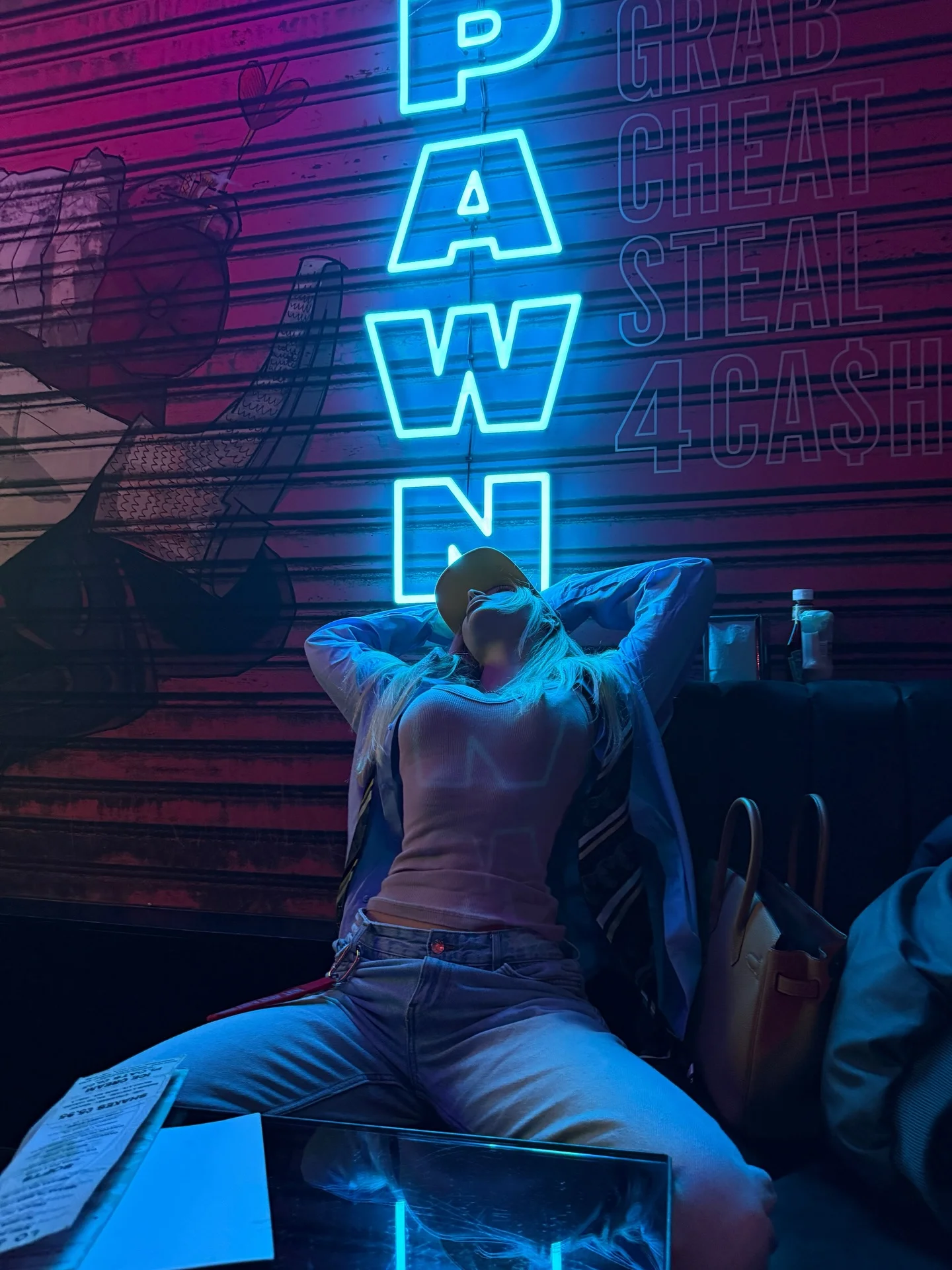 Person in a cap leaning back beneath blue and pink neon lights