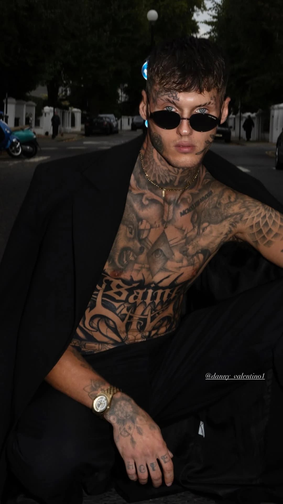 Tattooed man wearing dark sunglasses and a black blazer on a London street