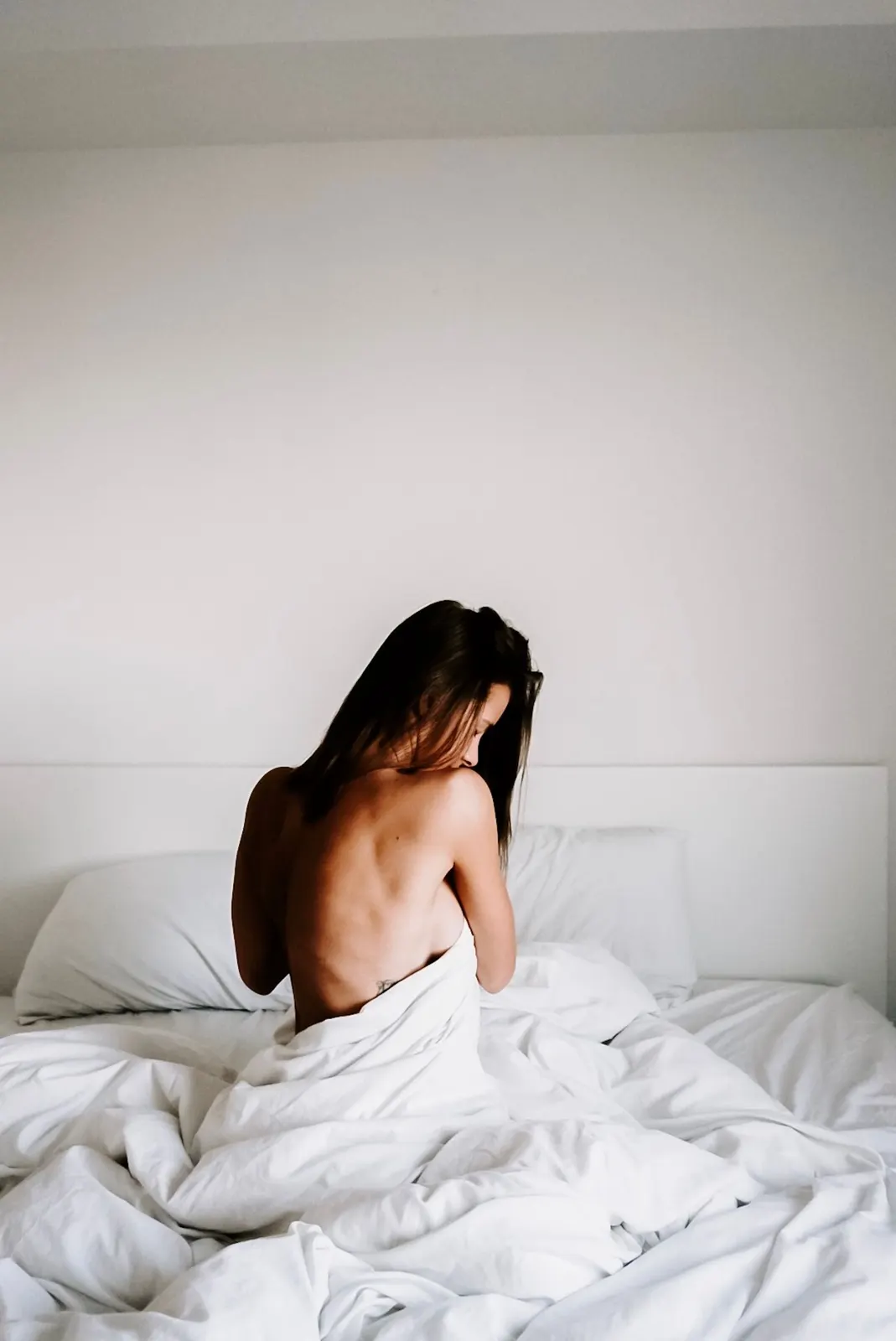 Woman seen from behind, sitting in a white duvet