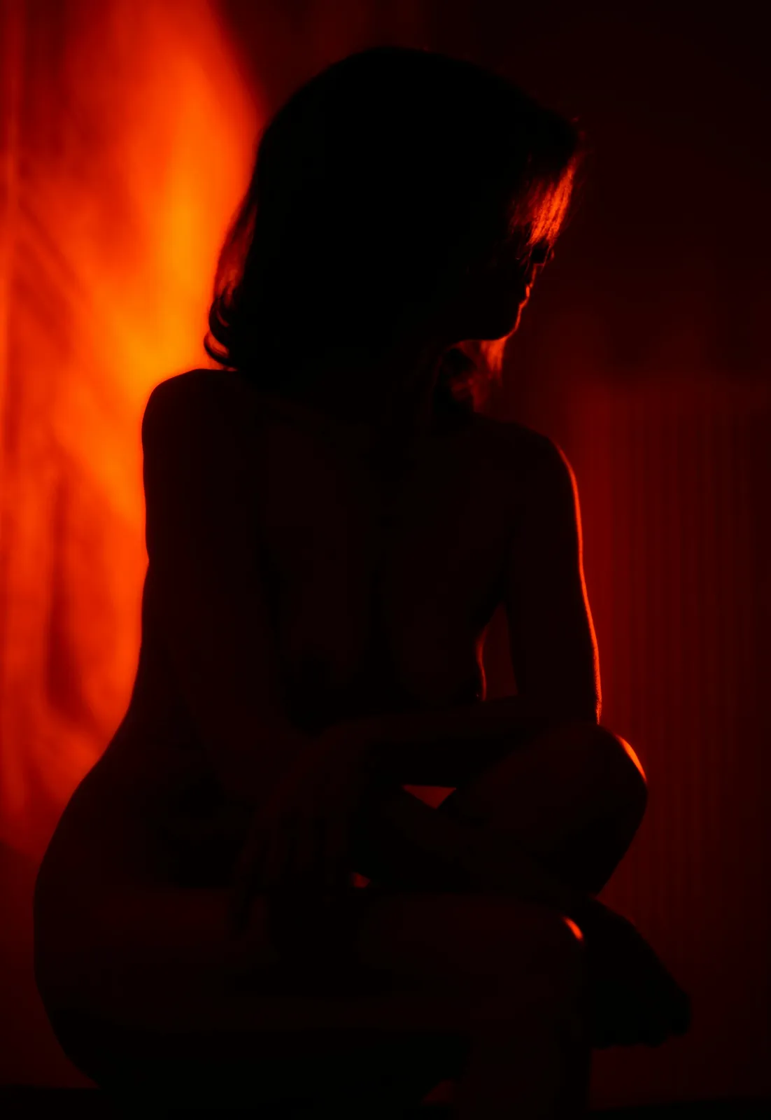 Silhouette of a woman sitting against a glowing red backdrop