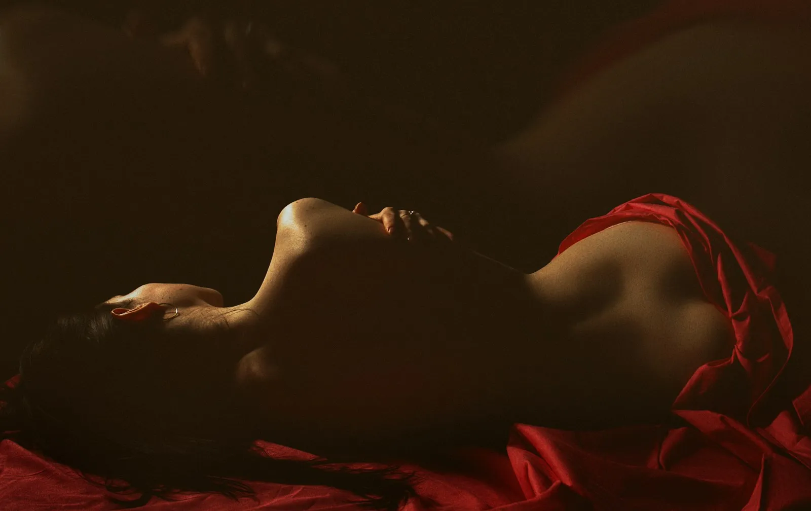 Woman lying on red silk in warm, low light