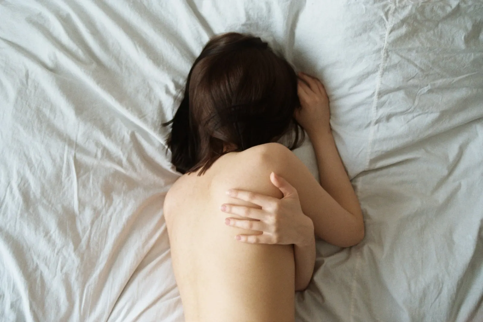 Woman lying face down on white sheets, her face hidden by her hair