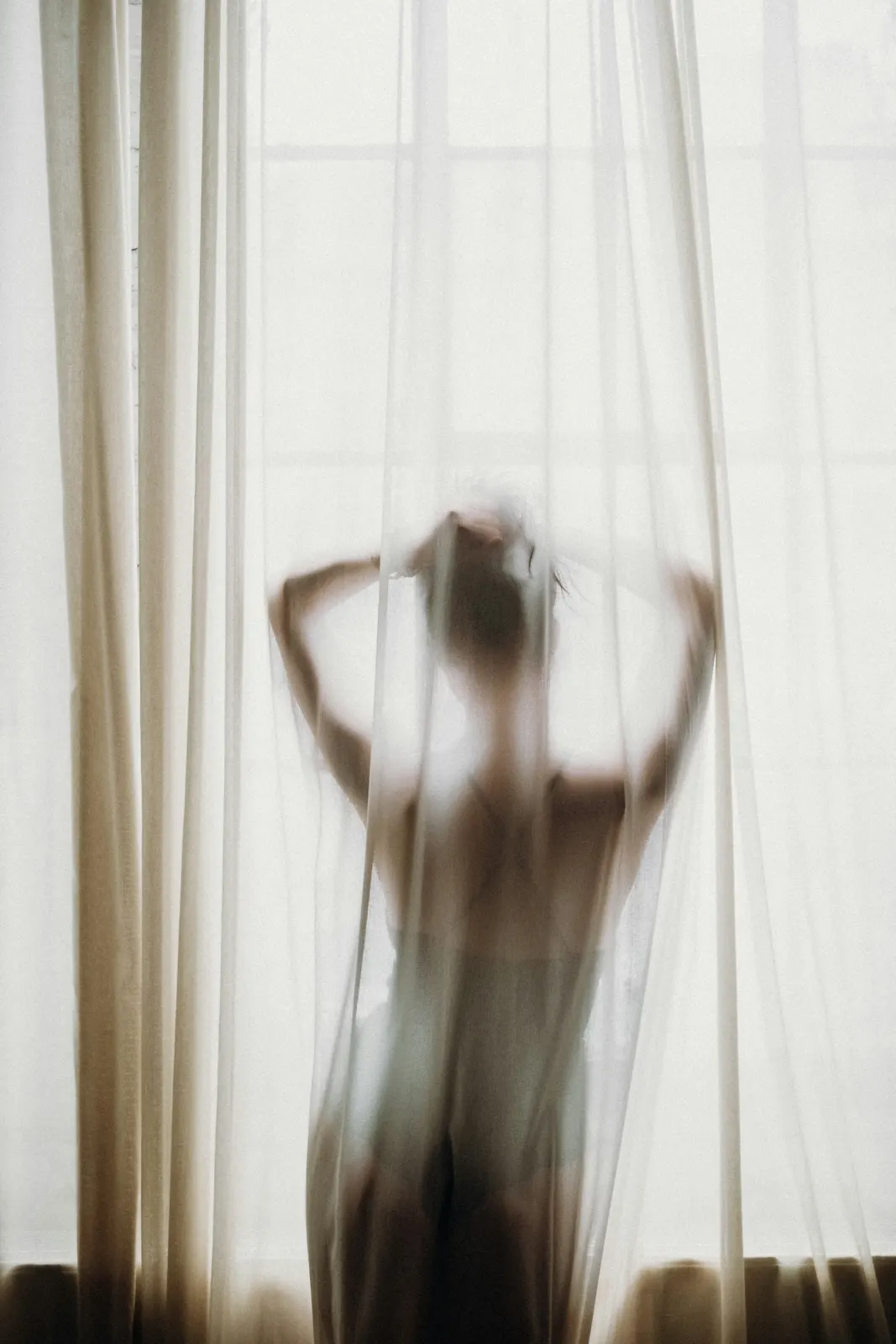 Silhouette of a woman behind a sheer white curtain