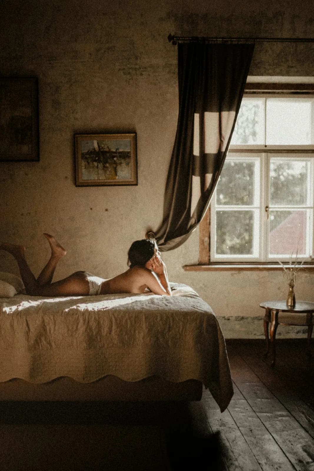 A quiet bedroom with a tall window and a woman resting on the bed